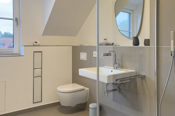 Helles Badezimmer unter der Dachschräge mit Fenster, Waschbecken und Glasdusche