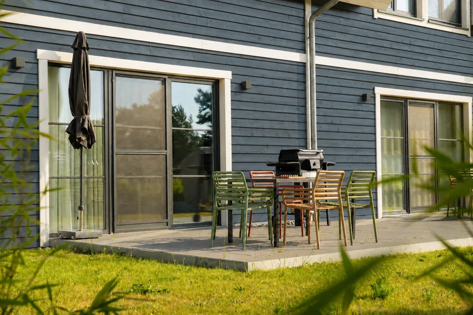 Sonnige Terrasse am Ferienhaus Lee mit Esstisch, bunten Stühlen und Grill